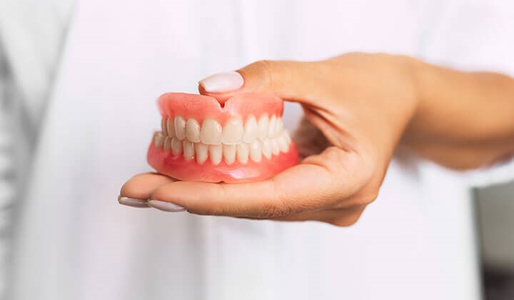 Woman holds dentures Prevent denture pressure points